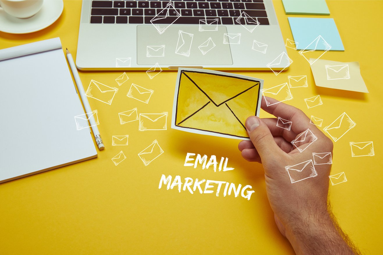 cropped image of man holding envelope sign near laptop with 'email marketing' lettering and email icons